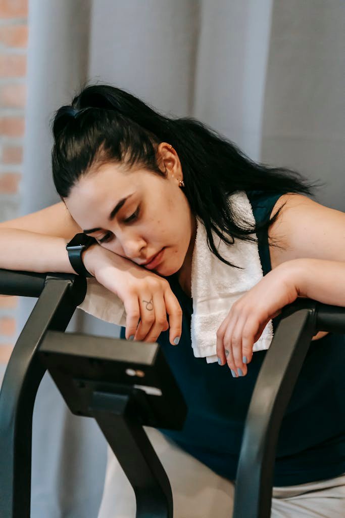 Tired woman with towel resting on gym machine, symbolizing workout fatigue and determination.